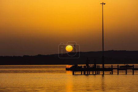 Téléchargez les photos : La pleine lune jaunâtre-orange rougeoyante sur un lac avec la silhouette des collines en arrière-plan - en image libre de droit