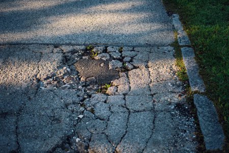 Photo for The cracked and damaged street near the green grass with sunlight shadow - Royalty Free Image