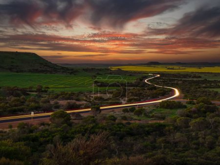 Téléchargez les photos : Un long plan d'exposition du coucher de soleil lumineux envoûtant sur la vallée de Chapman avec une route sinueuse éclairée par des sentiers lumineux des voitures - en image libre de droit
