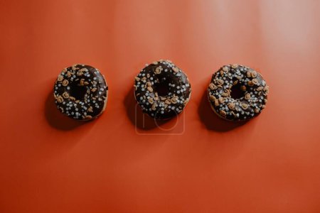 Foto de Una vista superior de donuts recién horneados, glaseados con chocolate y decorados con minúsculas linternas jack-o, sobre un fondo naranja - Imagen libre de derechos