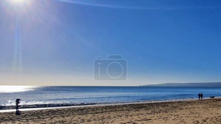 Téléchargez les photos : Vue panoramique de personnes marchant le long d'une plage sous un ciel clair et ensoleillé - en image libre de droit