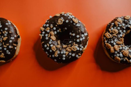 Photo for A top view of freshly baked donuts, glazed with chocolate and decorated with tiny jack-o-lanterns, on an orange background - Royalty Free Image