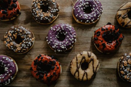 Photo for A closeup shot of freshly baked donuts, glazed with chocolate and vanilla, differently decorated, served on a wooden cutting board - Royalty Free Image