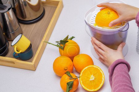 Photo for Woman's hands squeezing oranges in a juicer in her kitchen at home - Royalty Free Image