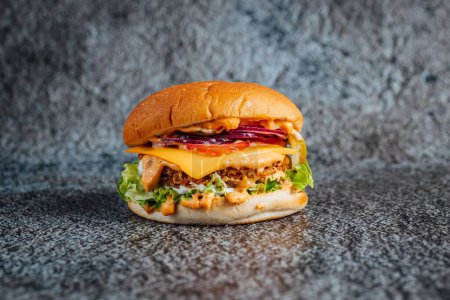 Foto de Un primer plano de una gran hamburguesa de carne de res con verduras en una superficie gris - Imagen libre de derechos