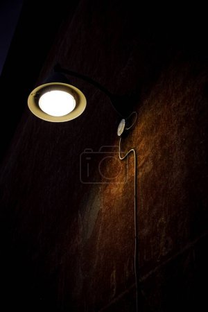 Foto de Un plano vertical de ángulo bajo de una lámpara que ilumina una pared oscura y vieja - Imagen libre de derechos