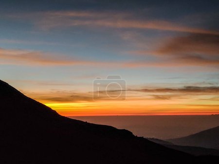 Foto de Una hermosa puesta de sol naranja sobre la silueta de una colina - Imagen libre de derechos