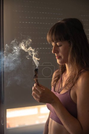 Photo for A vertical shot of a young Caucasian woman burning a palo santo to practice mindfulness - Royalty Free Image