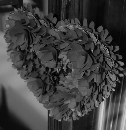 Téléchargez les photos : Un gros plan de fleurs en papier, en forme de couronne de cœur, sur un pas de porte en bois dans une maison, en niveaux de gris, le concept d'une décoration - en image libre de droit