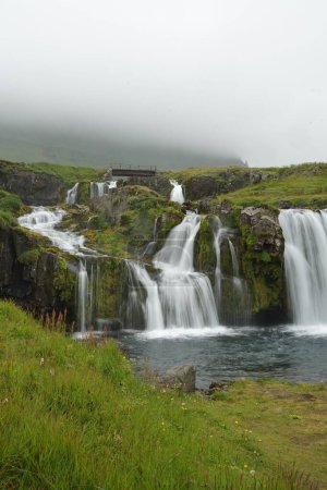 Photo for A beautiful scene of Kirkjufellsfoss waterfall with green grass on a cloudy day - Royalty Free Image