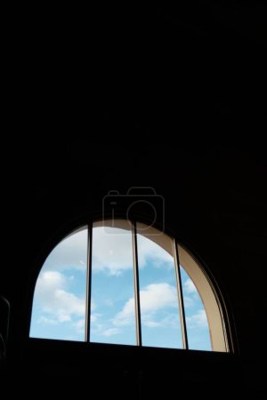 Foto de Una vertical de las nubes en el cielo azul vista desde una ventana semicircular y arqueada con protectores de ventanas - Imagen libre de derechos
