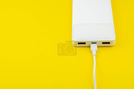 Téléchargez les photos : Une banque d'alimentation blanche avec un câble USB sur une surface jaune - en image libre de droit