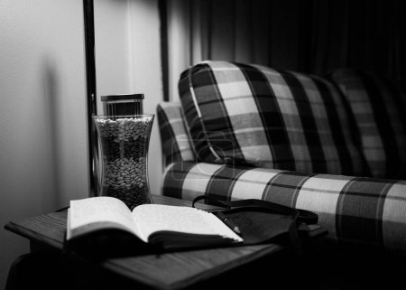 Foto de La vista a escala de grises de un libro abierto y un jarrón sobre una pequeña mesa junto al sillón - Imagen libre de derechos
