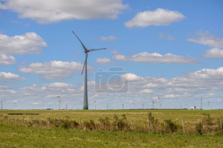Foto de Una turbina de viento solitaria bajo un cielo nublado y el horizonte lleno de molinos de viento en el campo de Uruguay - Imagen libre de derechos