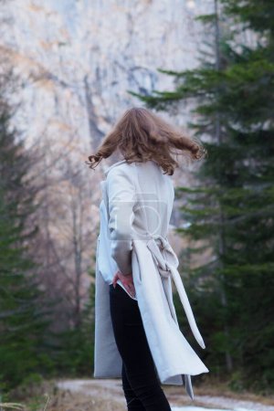 Photo for A vertical shot of a young Caucasian female walking in a forest wearing a white coat - Royalty Free Image