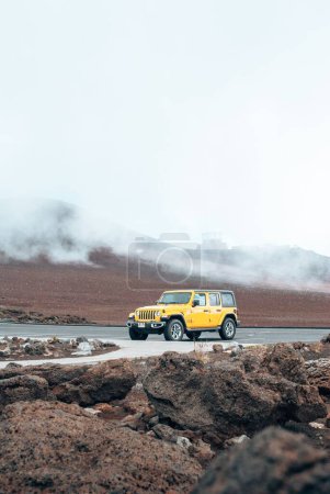 Téléchargez les photos : Plan vertical d'une Jeep jaune sur une route avec un fond de volcans dans le parc national Haleakala - en image libre de droit