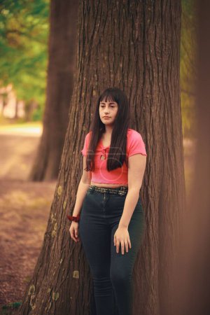 Foto de Una foto vertical de una hermosa joven parada detrás de un árbol en un bosque - Imagen libre de derechos