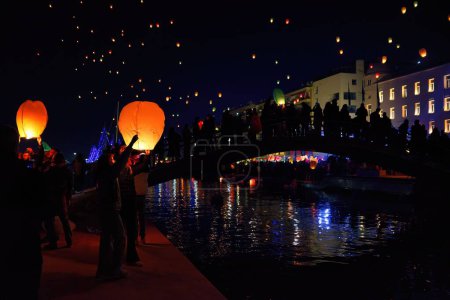 Téléchargez les photos : Un groupe de personnes relâchant des lanternes de ciel lumineux pour célébrer les lumières et faire des vœux à Volos, Grèce - en image libre de droit