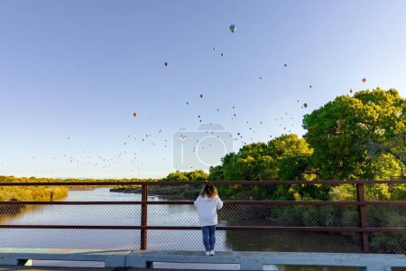 Téléchargez les photos : Une dame devant une clôture métallique regardant des montgolfières au-dessus d'Albuquerque, Nouveau-Mexique, États-Unis - en image libre de droit
