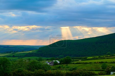 Foto de Una vista panorámica de los rayos brillantes de la luz del sol rompiendo a través de las nubes sobre montañas de hoja perenne en Cumbria - Imagen libre de derechos