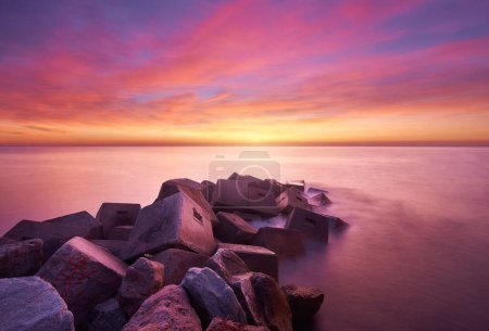 Foto de Un dramático disparo de rocas junto al mar en una puesta de sol rosada - Imagen libre de derechos