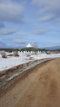 Foto de Un plano vertical de un camino de tierra con lados nevados y la escuela Bigstone con sus techos cónicos en el fondo - Imagen libre de derechos