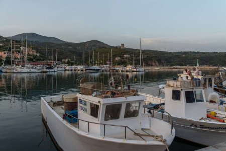 Téléchargez les photos : Une image de bateaux de pêche garés dans le port de Marina di Camerota lors d'un coucher de soleil avec des montagnes sur le fond - en image libre de droit