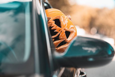 Photo for A closeup shot of a young man with a pumpkin on his head riding a car - Royalty Free Image