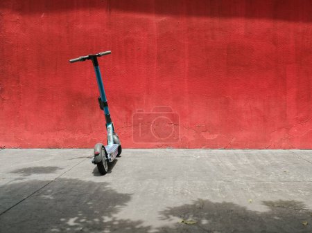 Foto de Un primer plano de un scooter eléctrico estacionado contra una pared roja brillante en las calles - Imagen libre de derechos