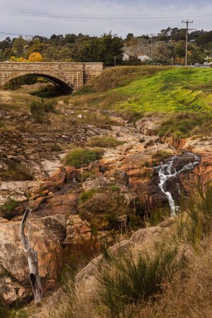 Foto de Un disparo vertical de un viejo puente de piedra sobre un arroyo, hierba y rocas en Bright Victoria, Australia - Imagen libre de derechos