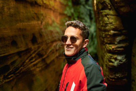 Téléchargez les photos : Un homme hispanique avec des lunettes de soleil souriant et debout entre les grottes - en image libre de droit