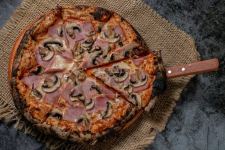 Foto de Vista superior de una pizza napolitana cocida en horno de leña, servida sobre un mantel de paja - Imagen libre de derechos