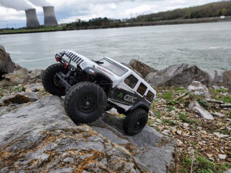 Photo for A toy car Jeep Wrangler on stones by the lake with a view of nuclear power plant - Royalty Free Image