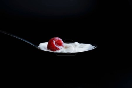 Foto de Frambuesa salpicadura de leche en una cuchara de metal efecto salpicadura con fondo negro - Imagen libre de derechos