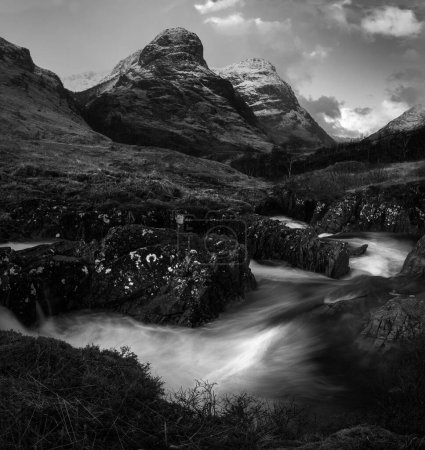 Téléchargez les photos : Vue en noir et blanc d'une rivière à longue exposition qui coule à travers des champs montagneux - en image libre de droit