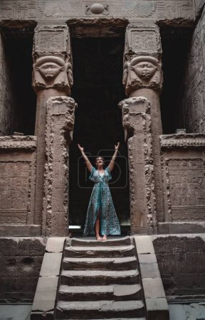 Foto de Una hermosa mujer caucásica descalza en un vestido azul que explora el Templo de Hathor. Dendera, Egipto. - Imagen libre de derechos