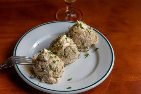 Photo for A closeup shot of German Bread Dumplings sprinkled with parsley and chive and served on a ceramic plate with a fork and a glass in the background - Royalty Free Image