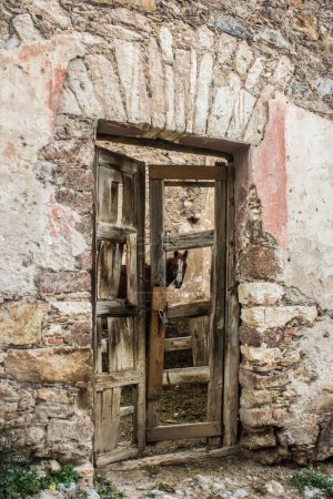 Téléchargez les photos : Un cheval brun (Equus caballus) vu depuis une porte verrouillée en bois d'un bâtiment en pierre altérée dans un village - en image libre de droit