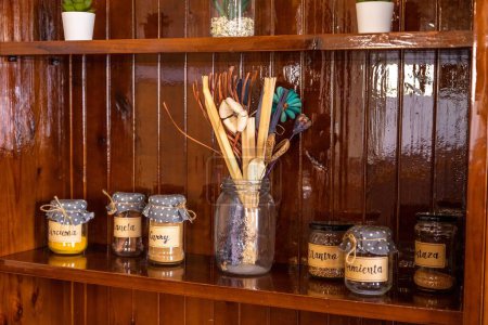 Photo for Labeled jars with spices, with dotted cloths on lids, on a shiny wooden shelf, with artificial flowers, spoons, and straws in a bigger jar - Royalty Free Image