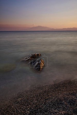 Téléchargez les photos : Une verticale de vagues de mer contre une plage rocheuse au coucher du soleil prise en longue exposition - en image libre de droit