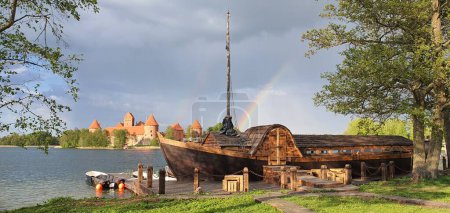 Téléchargez les photos : Un vieux bateau en bois sur un quai avec le château de l'île de Trakai et un arc-en-ciel en arrière-plan - en image libre de droit