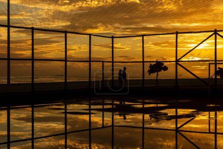Téléchargez les photos : Silhouette de personnes s'exerçant sur le bord de la plage du Rio Vermelho à Salvador, Bahia, contre le coucher de soleil jaune. - en image libre de droit