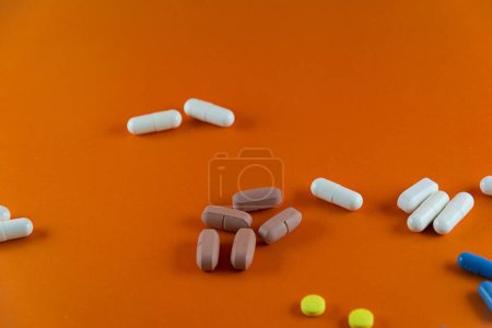 Foto de Diferentes píldoras de color marrón blanco azul y amarillo dispersas sobre fondo de color naranja. Material médico. - Imagen libre de derechos