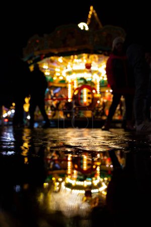 Téléchargez les photos : Un plan vertical flou d'un carrousel avec ses lumières allumées et les gens autour dans un parc d'attractions la nuit - en image libre de droit