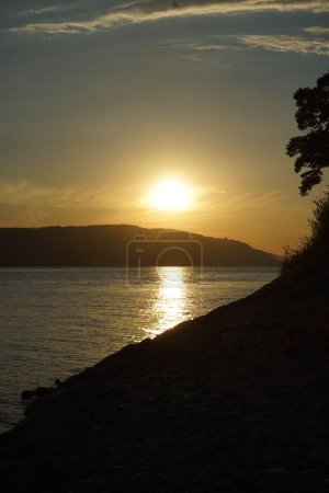 Photo for A vertical shot of the sunset over the lake with hills in the background - Royalty Free Image
