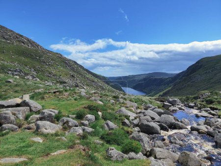 Téléchargez les photos : Un gros plan de pierres, de montagnes et d'une rivière au loin dans le parc national Glendalough - en image libre de droit
