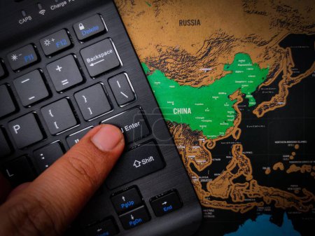Téléchargez les photos : Un gros plan d'un doigt appuyant sur "Entrée" sur un clavier noir sur le dessus de la carte de la Chine - concept d'entreprise - en image libre de droit