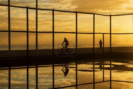 Téléchargez les photos : Salvador, Bahia, Brésil - 05 décembre 2021 : Cycliste faisant de l'exercice sur le bord de la plage du Rio Vermelho contre le coucher du soleil. Ville de Salvador, Bahia. - en image libre de droit