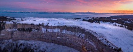 Téléchargez les photos : Une vue panoramique de quelques rochers avec des arbres couverts de neige avec coucher de soleil rose dessus - en image libre de droit