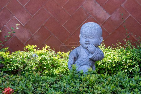Téléchargez les photos : Une statue de bébé Bouddha dans le jardin entouré de plantes - en image libre de droit